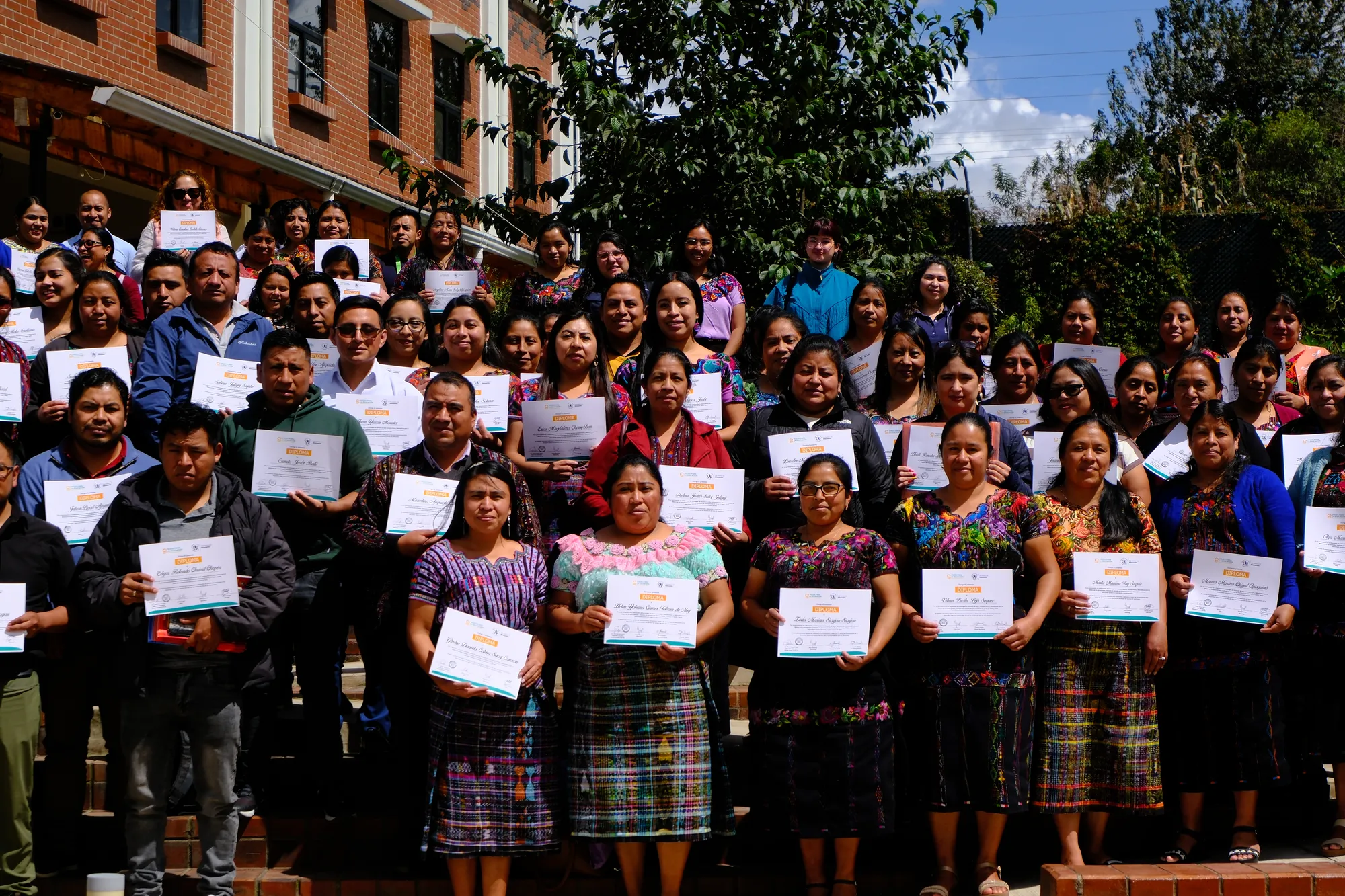 Decenas de docentes posan al aire libre sosteniendo sus diplomas.